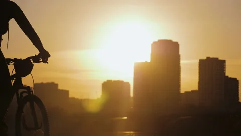 Silhouette of two cyclists riding on background of urban buildings during sunset Stock Footage 130213045