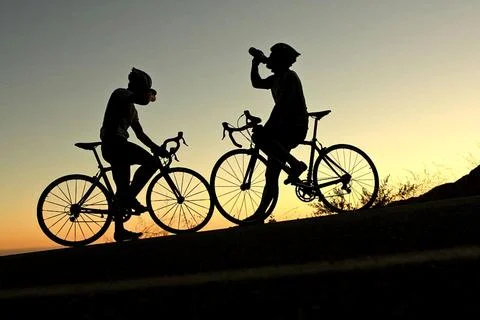 Silhouette of two cyclists taking a break during a ride at sunset Stock Photos