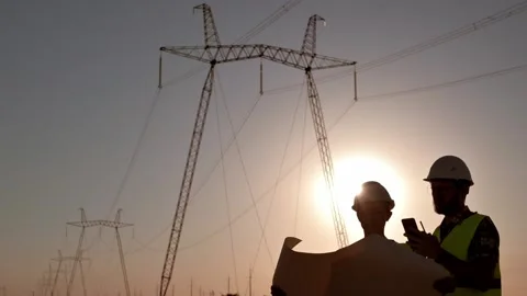 Silhouette of two electrical engineers in hard hats standing in field at sunset Stockbeeldmateriaal 201032224