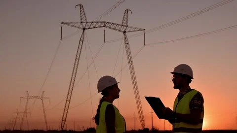 Silhouette of two electrical engineers in hard hats standing in field at sunset Stockbeeldmateriaal 206033717
