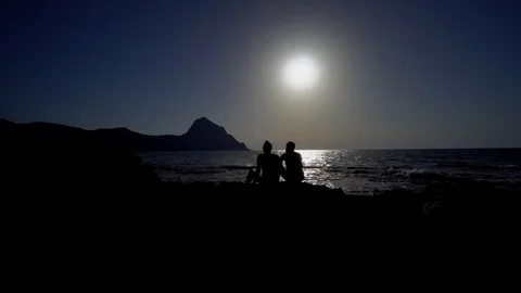 Silhouette of two lovers seated on the rocks by the sea. Stock Footage 93789815