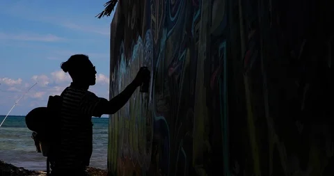 Silhouette Of Two Men Creating A Graffiti Mural Next To The Beach Stock Footage 102588374
