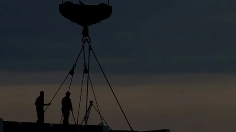 Silhouette of two men working with crane hook and chains on construction site at Stock Footage 326748638