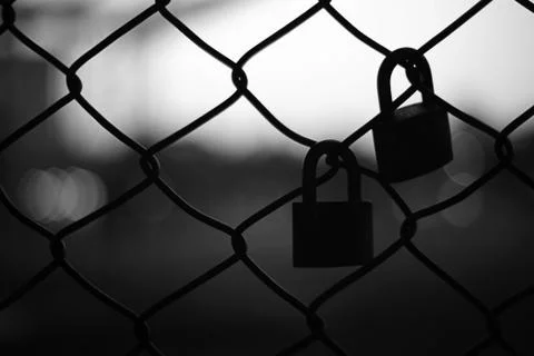 Silhouette of two pad locks on chain link fence Stock Photos