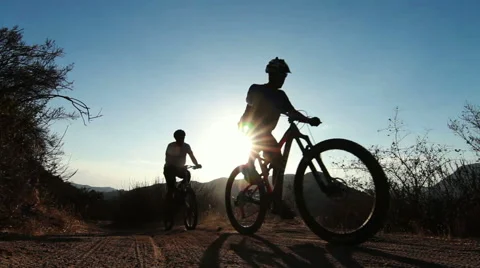 Silhouette Two People Mountain Bike Riding At Sunset Stock Footage