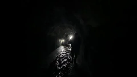 The silhouette of two people walking through a wet, dark tunnel. Stock Footage 273192418