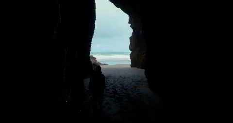 Silhouette of two people walking through a large dark cave into the light. Piha, Stock Footage 286074169
