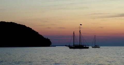 Silhouette of two sailboats with sails down approaching shore at dusk. Stock Footage 254928909