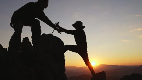 Silhouette of two tourists lends helping hand climb cliffs mountains Stock Footage 336932843