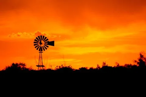 Silhouette of a windmill in front of a bright orange sunset. Foto stock