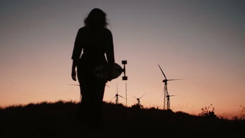 Silhouette on windmill generators in sunset near a pretty girl with skateboard Stock Footage 143784343