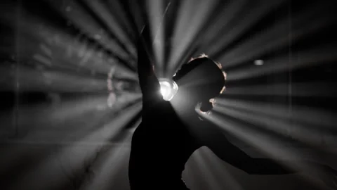 Silhouette of a woman dancing with dramatic light rays and smoke in a dark Stock Footage 344908242