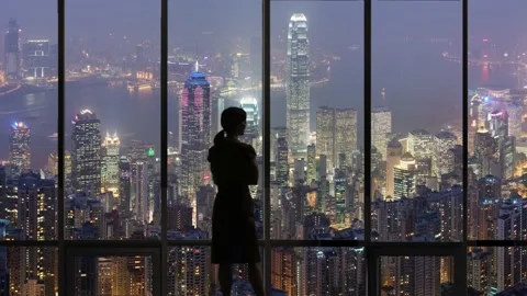 A Silhouette woman looking out office window at hong kong night skyline Stock Footage