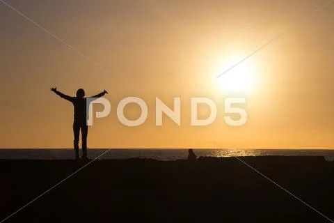 Silhouette of woman raising hands to sun at sunset. Stock Photos