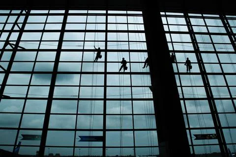 A silhouette of a worker cleaning windows hangs from a rope in the airport .. Foto stock