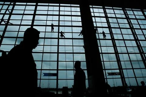 A silhouette of a worker cleaning windows hangs from a rope in the airport .. Stock Photos