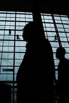 A silhouette of a worker cleaning windows hangs from a rope in the airport .. Foto stock