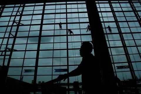 A silhouette of a worker cleaning windows hangs from a rope in the airport .. Stock Photos