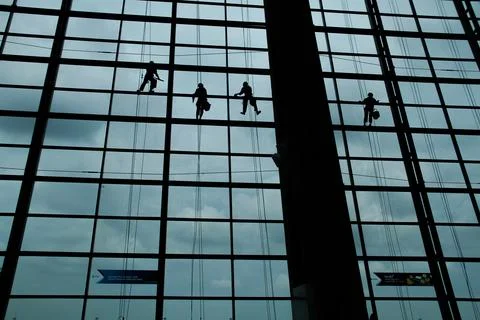 A silhouette of a worker cleaning windows hangs from a rope in the airport .. Stock Photos