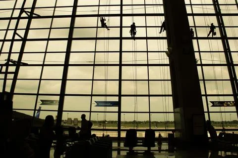 A silhouette of a worker cleaning windows hangs from a rope in the airport .. Stock Photos