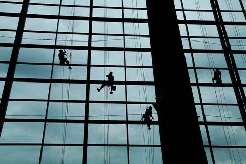 A silhouette of a worker cleaning windows hangs from a rope in the airport .. Foto stock
