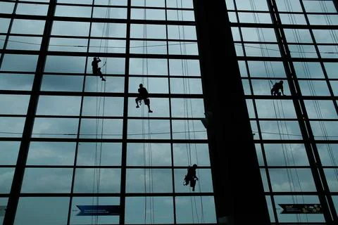A silhouette of a worker cleaning windows hangs from a rope in the airport .. Stock Photos