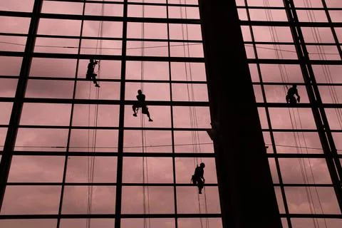 A silhouette of a worker cleaning windows hangs from a rope in the airport .. Stock Photos
