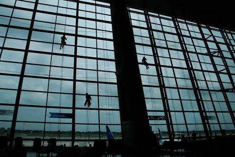 A silhouette of a worker cleaning windows hangs from a rope in the airport .. Stock Photos