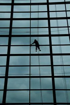 A silhouette of a worker cleaning windows hangs from a rope in the airport .. Stock Photos