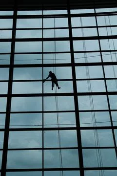A silhouette of a worker cleaning windows hangs from a rope in the airport .. Stock Photos