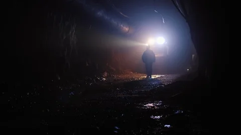 Silhouette of a worker with headlamp walking through a mine dark tunnel Stock Footage 116502836