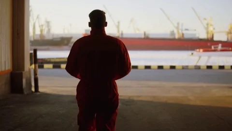 Silhouette of a worker in orange uniform walking through the harbour storage by Stock Footage 73296601