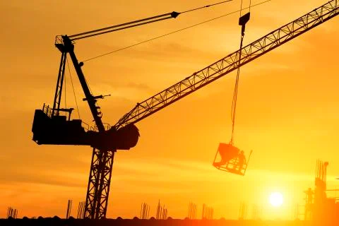 Silhouette workers working on cranes on construction sites at sunset. Stock Photos