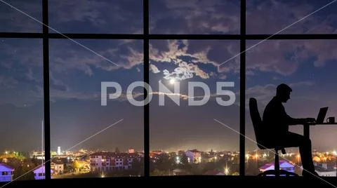 The silhouette of working man near window on the night city background Stock Photos