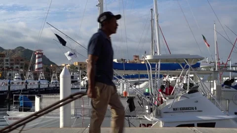 Silhouette of working man walking passed boats at pier with a loading dolly Stock Footage 248477312