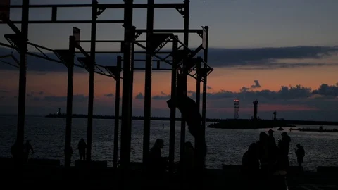 Silhouette workout by the sea pulling up on horizontal bar at sunset Stock Footage 127177747