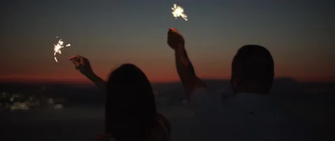 Silhouette of young couple celebrating while holding sparklers at sunset Stock Footage 136240624