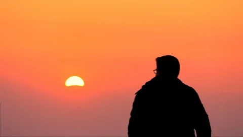 Silhouette of a young guy looking at an orange Sunset Vidéo 84740160