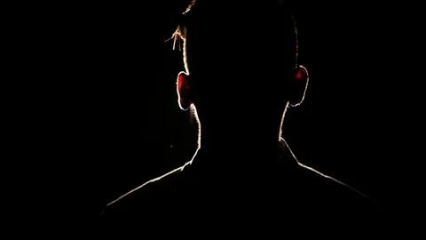 Silhouette of young guy slightly shaking his head in the darkness. Bright lamp Видео 106470959