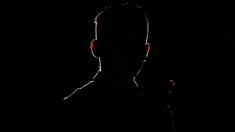 Silhouette of young guy with smartphone in hand in the darkness. Bright lamp Video stock 106470985