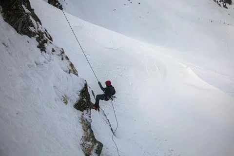 Silhouette of young man abseiling down from a snowy cliff. Climber rappelli.. Stock Photos