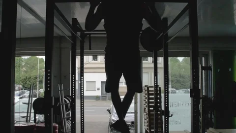 Silhouette of a young man doing pull-up exercise on a horizontal bar at gym Stock Footage 114295400