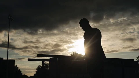 Silhouette of a young man exercising push-ups on parallel bars outdoors. Bottom Stock Footage 120440996