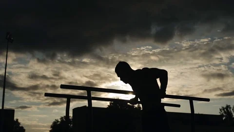 Silhouette of a young man exercising push-ups on parallel bars outdoors. Bottom Stock Footage 120441135