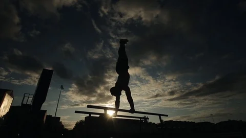 Silhouette of a young man exercising push-ups on parallel bars outdoors. Bottom Stock Footage 120508016