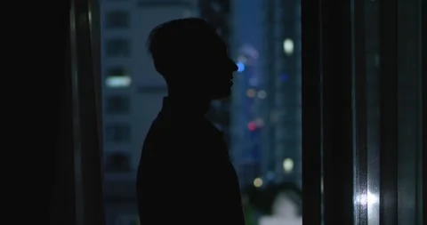 Silhouette of young man standing by window in dark with beautiful view of Stock Footage 264323136