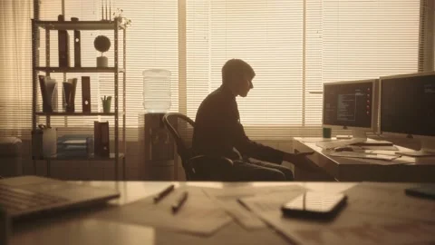 Silhouette of a young man takes a folder with documents and typing on a computer Stock Footage 239023708