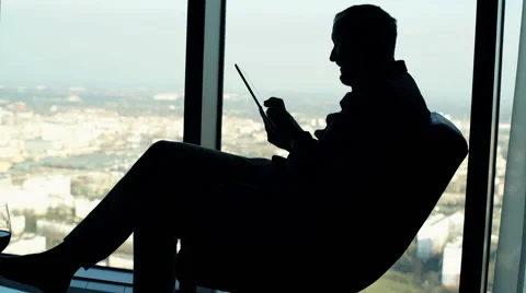 Silhouette of young man using tablet computer sitting on armchair by the window Stock Footage 63220778