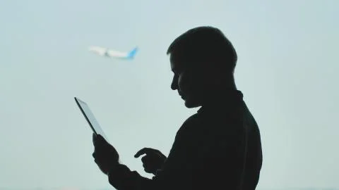 Silhouette of young men using tablet pc on the background of an airplane taking Stock Photos