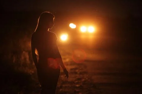 Silhouette of young slender woman in the backlight of car headlights on the r Stock Photos